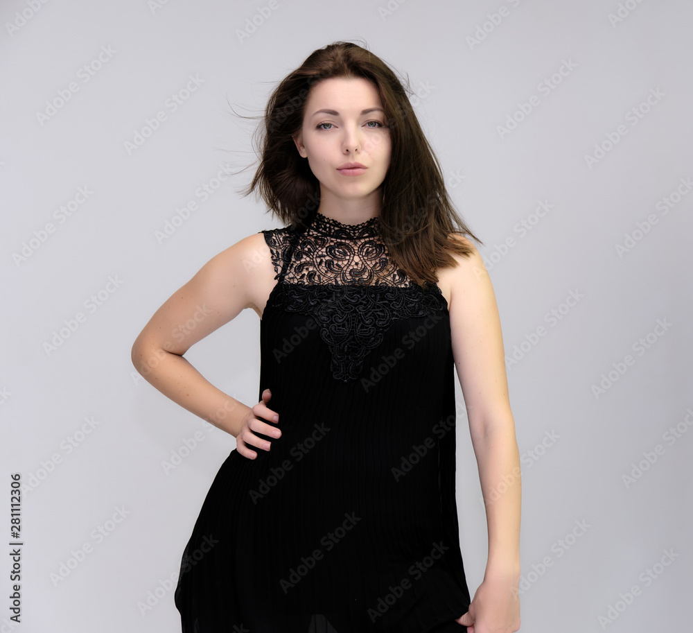 A portrait above the knee of a pretty beautiful fashionable adult brunette girl in a black dress on a white background. Standing right in front of the camera, showing different poses and emotions. A portrait above the knee of a pretty beautiful fashionable adult brunette girl in a black dress on a white background. Standing right in front of the camera, showing different poses and emotions.