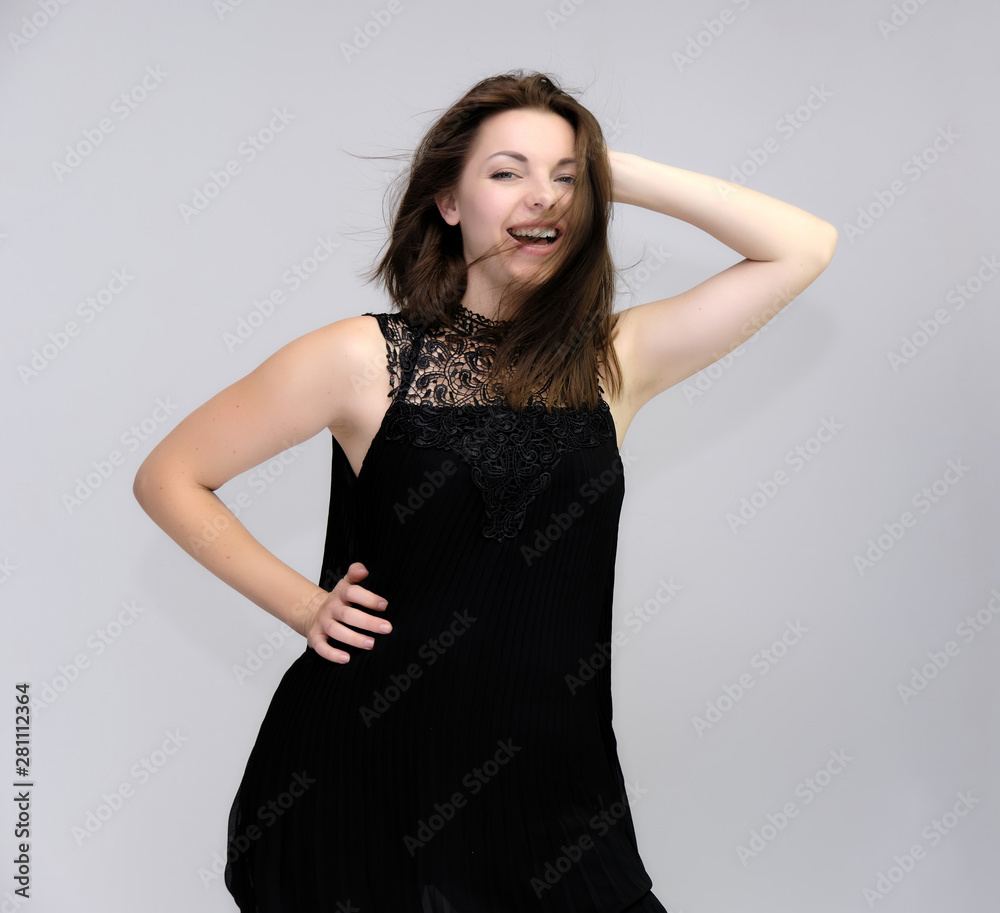 A portrait above the knee of a pretty beautiful fashionable adult brunette girl in a black dress on a white background. Standing right in front of the camera, showing different poses and emotions. A portrait above the knee of a pretty beautiful fashionable adult brunette girl in a black dress on a white background. Standing right in front of the camera, showing different poses and emotions.