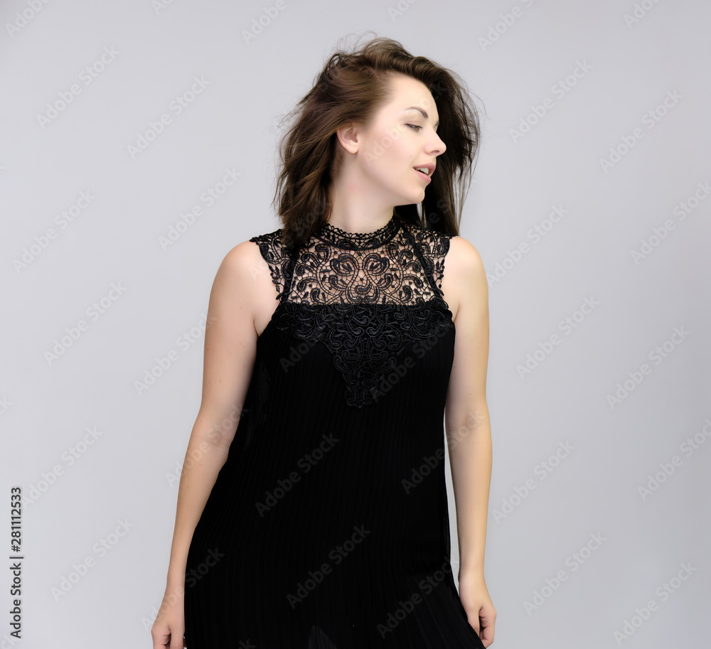 A portrait above the knee of a pretty beautiful fashionable adult brunette girl in a black dress on a white background. Standing right in front of the camera, showing different poses and emotions. A portrait above the knee of a pretty beautiful fashionable adult brunette girl in a black dress on a white background. Standing right in front of the camera, showing different poses and emotions.