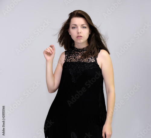 A portrait above the knee of a pretty beautiful fashionable adult brunette girl in a black dress on a white background. Standing right in front of the camera, showing different poses and emotions.