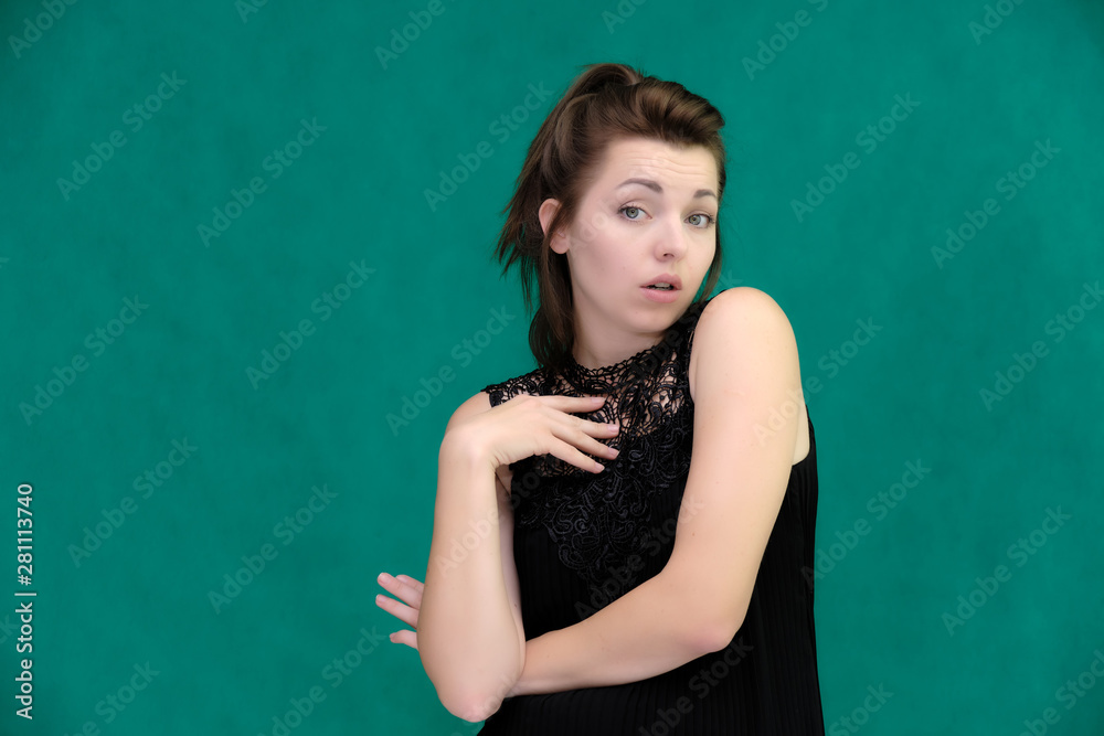 Portrait of a pretty beautiful fashionable adult brunette girl in a black dress on a green background. Standing right in front of the camera, showing different poses and emotions.
