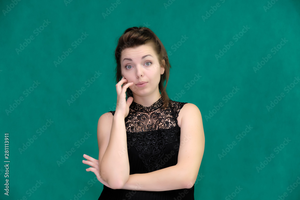 Portrait of a pretty beautiful fashionable adult brunette girl in a black dress on a green background. Standing right in front of the camera, showing different poses and emotions. Portrait of a pretty beautiful fashionable adult brunette girl in a black dress on a green background. Standing right in front of the camera, showing different poses and emotions.
