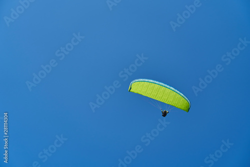 A paraglider with a yellow-green parachute sailing accros a clear, cloudless blue sky. Extreme, adrenaline sports. A lot of negative space for messages. photo