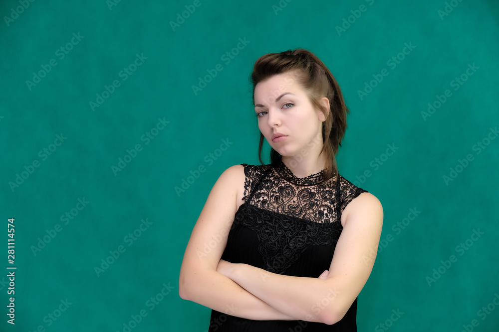 Portrait of a pretty beautiful fashionable adult brunette girl in a black dress on a green background. Standing right in front of the camera, showing different poses and emotions. Portrait of a pretty beautiful fashionable adult brunette girl in a black dress on a green background. Standing right in front of the camera, showing different poses and emotions.