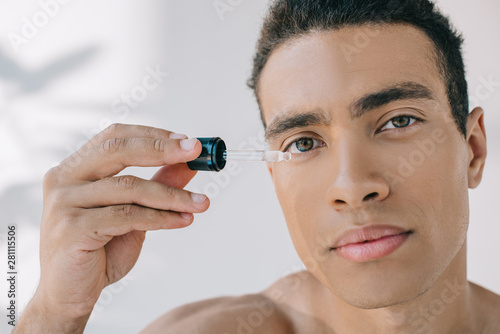 portrair shot of mixed race man holsing pipette with serum and looking at camera photo