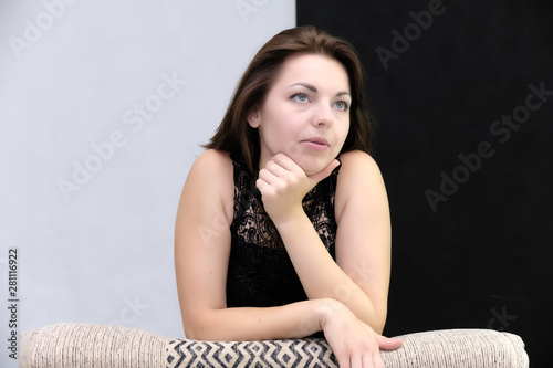 Portrait of a pretty beautiful fashionable adult brunette girl in a black dress. Sits on the sofa right in front of the camera, talking demonstrating different poses and emotions
