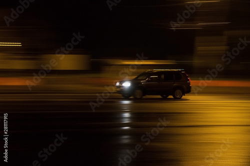 The car goes at night at high speed on a wet road.