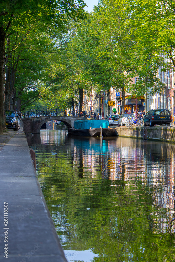 Amsterdam, Netherlands - 06/14/2019: canal with bridge and boats in Amsterdam, Netherlands. Traditional dutch cityscape. Historic street in Amsterdam with boats and tourists. Summer travel concept.