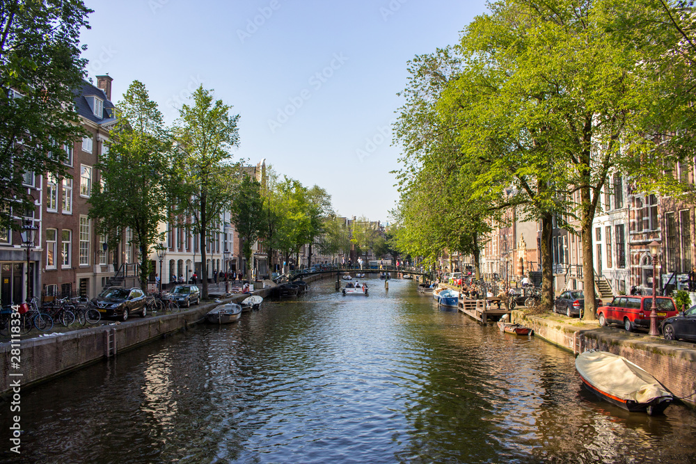 Fototapeta premium Amsterdam, Netherlands - 06/14/2019: canal with bridge and boats in Amsterdam, Netherlands. Traditional dutch cityscape. Historic street in Amsterdam with boats and tourists. Summer travel concept.