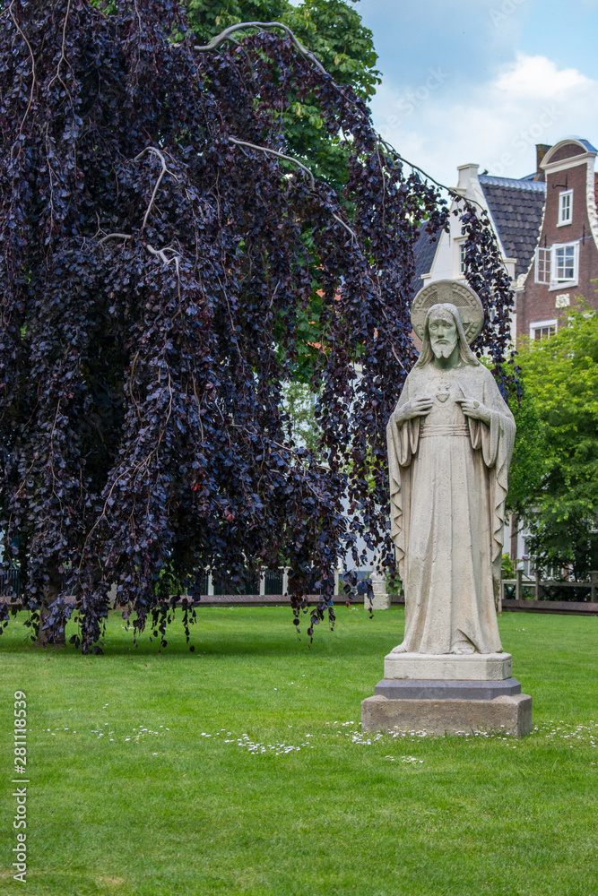 Obraz premium Amsterdam, Netherlands - 06/14/2019: garden of Begijnhof with ancient Jesus Christ statue. Famous medieval yard with sculpture of Jesus Christ in Amsterdam. Religious heritage.