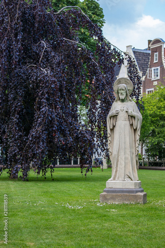 Amsterdam, Netherlands - 06/14/2019: garden of Begijnhof with ancient Jesus Christ statue. Famous medieval yard with sculpture of Jesus Christ in Amsterdam. Religious heritage. 