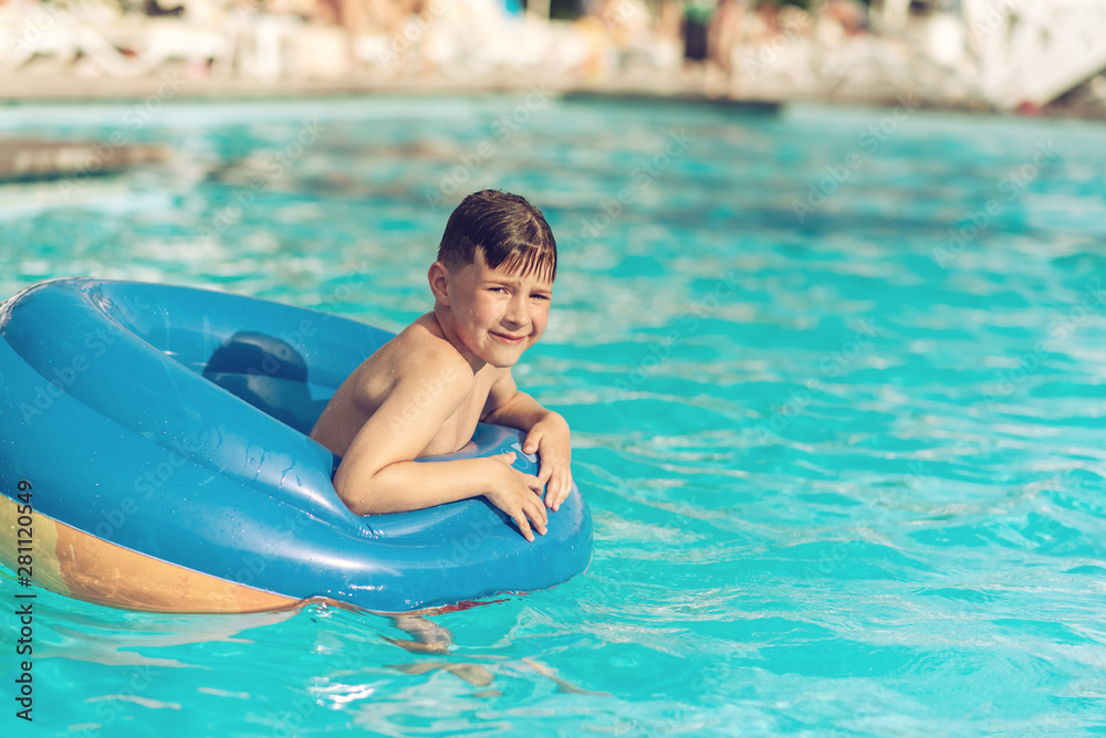 Portrait of happy European boy swimming in rubber ring in pool on summer vacation.
