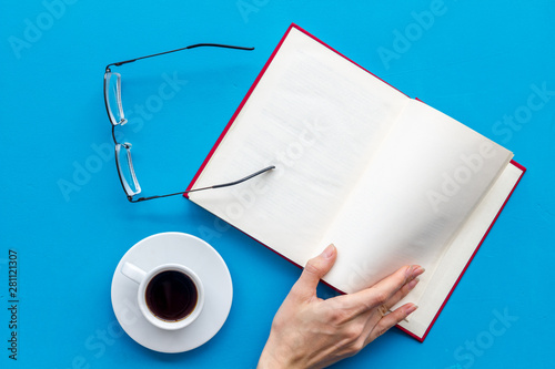 workplace with book in hands for reading, glasses, coffee on blue background flatlay mockup