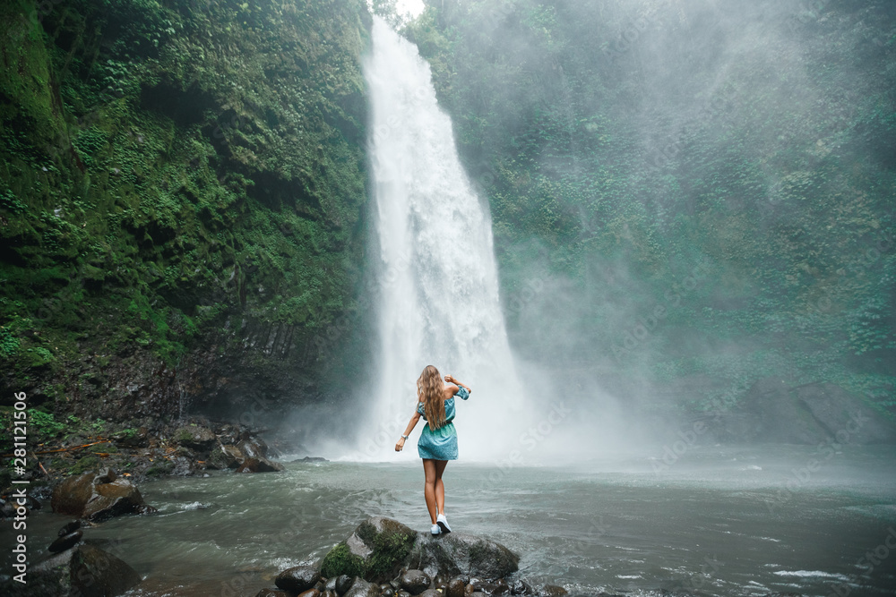 Obraz premium Back view young woman tourist enjoying tropical waterfall view in jungle