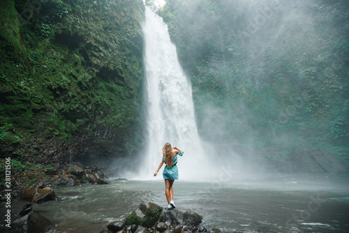 Back view young woman tourist enjoying tropical waterfall view in jungle
