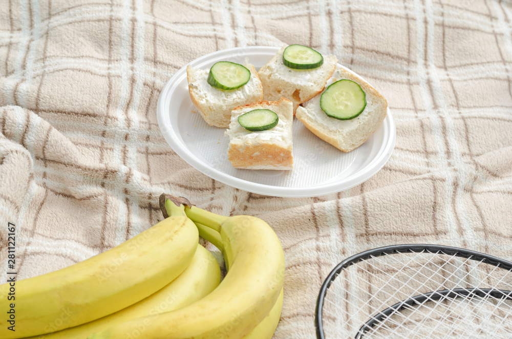 A Bunch of bananas ,badminton rackets and small summer sandwiches in the center for summer family sport picnic. A Bunch of bananas ,badminton rackets and small summer sandwiches in the center for summer family sport picnic.