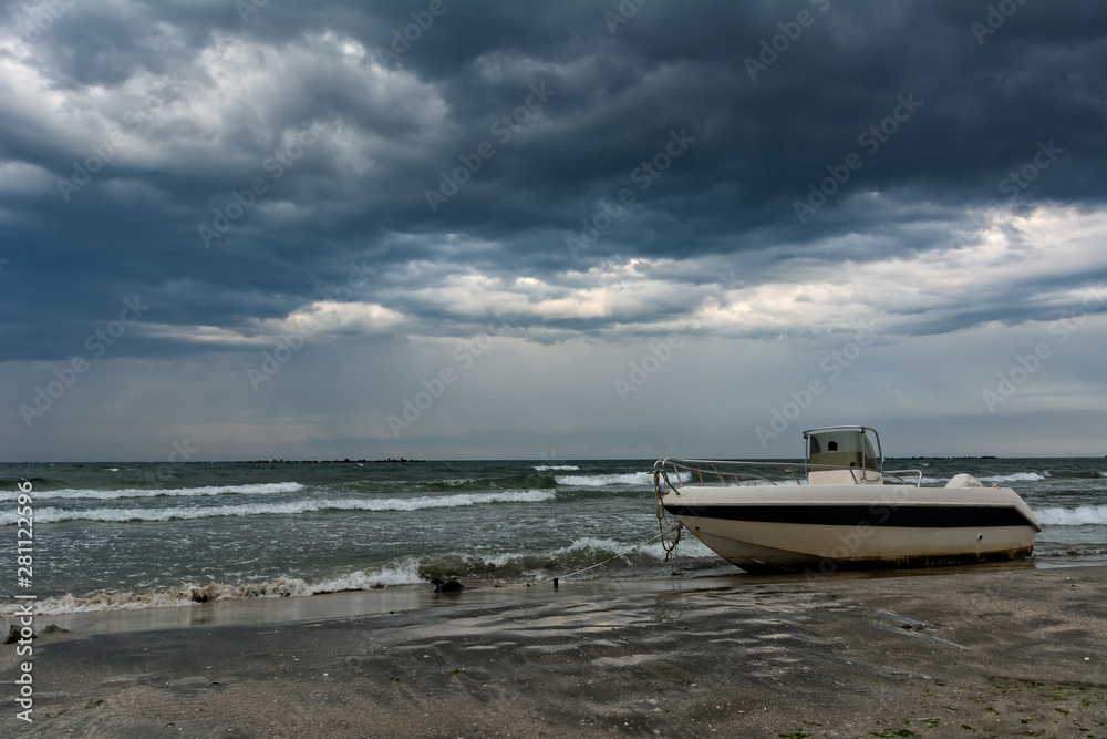 Small boat tied on the seashore and heavy thunderstorm clouds on the sky Small boat tied on the seashore and heavy thunderstorm clouds on the sky