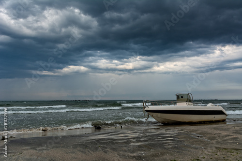 Small boat tied on the seashore and heavy thunderstorm clouds on the sky