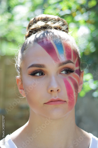 Beautiful young woman with a make-up shaped multicolored sunbeam. Hairstyle in a bun, blond and light red hair. Girl false eyelashes on the eyes and looking on the side. 