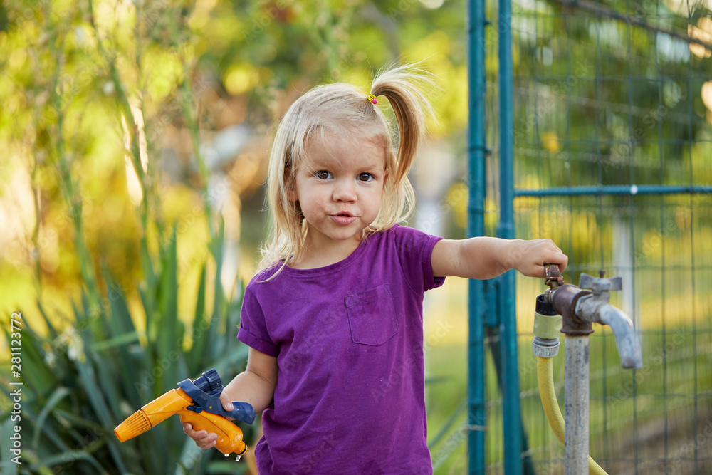 Cute little girl watering flowers in the garden at summer day. Child