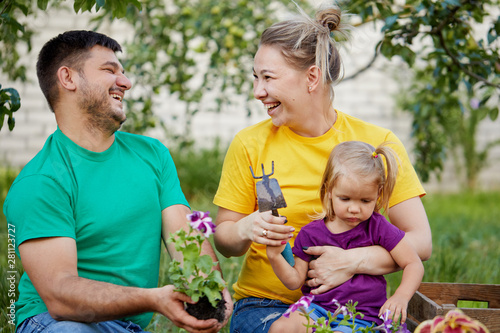 Happy family gardening together and taking care of nature. Plant sprouts and fertilize the ground. Mother, father and little child in colorful bright t-shirts in kailyard photo