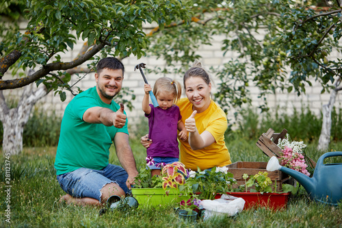 Happy family gardening together and taking care of nature. Plant sprouts and fertilize the ground. Mother, father and little child in colorful bright t-shirts in kailyard photo