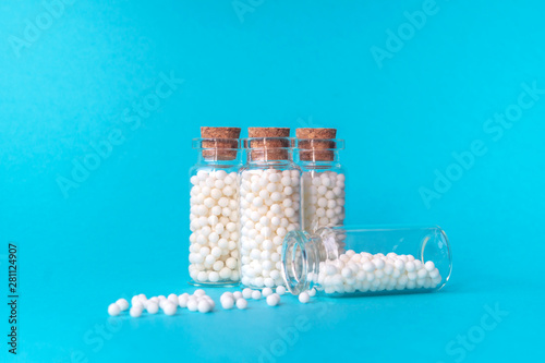 Homeopathic globules in four glass bottles on blue background. The globules are scattered from one bottle. Alternative homeopathy medicine herbs, healthcare and pills concept. Copy space for text photo