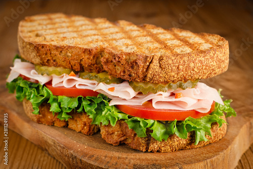handmade tasty turkey sandwich with tomato, salad and cucumber, on wooden background