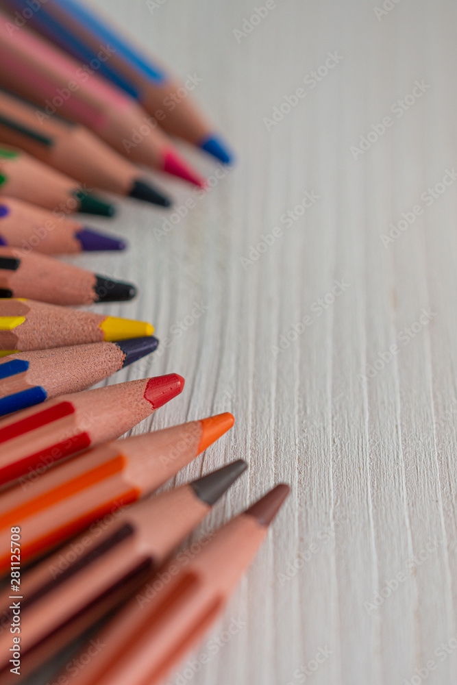 Defocused foreground, focused center and unfocused background of several colored pencils for school, in semicircle, on white wood in horizontal Defocused foreground, focused center and unfocused background of several colored pencils for school, in semicircle, on white wood in horizontal