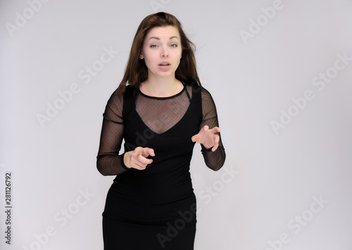 Portrait on white background of a pretty slim beautiful fashionable adult girl with beautiful brunette hair in a black dress. Standing talking demonstrating different poses and emotions