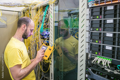  The system administrator is testing the network with a reflectometer. The man works in the server room of the datacenter. A technician measures the signal level in a fiber optic cable. photo