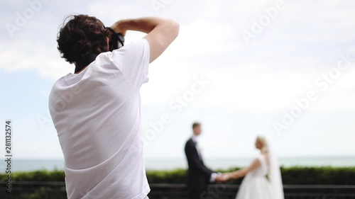 professional photographer  makes photos of wedding couple, blue sky background, backside view