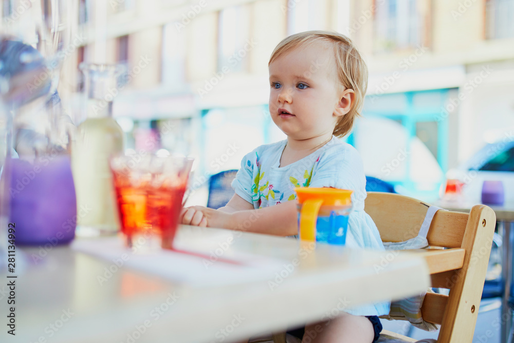 Adorable toddler girl sitting in high chair in cafe or restaurant Adorable toddler girl sitting in high chair in cafe or restaurant