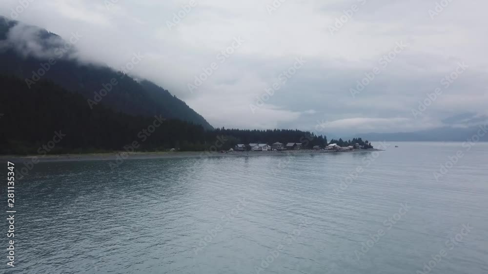 Aerial flyover view by DJI drone of a rocky shore with houses, boreal forest and the Kenai Mountains in the background near Seward Alaska on a cloudy day Aerial flyover view by DJI drone of a rocky shore with houses, boreal forest and the Kenai Mountains in the background near Seward Alaska on a cloudy day