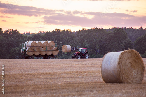 Tractor loading bales of straw on a trailer in the sunset