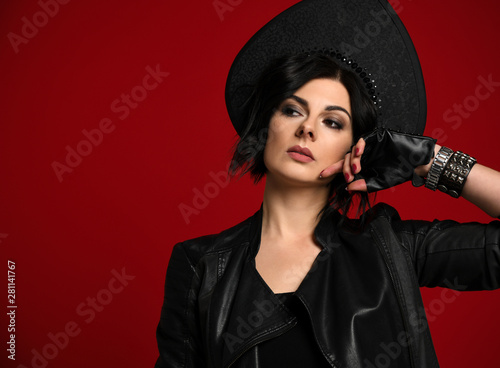 Sexy and brutal woman brunette in stylish neofolk clothes black leather jacket and black kokoshnik looks askance on red