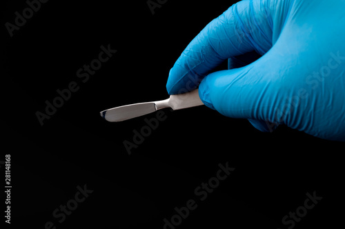 Surgical instruments in operating room and doctor performing surgery concept theme with a surgeon hand wearing blue latex gloves and holding a scalpel isolated on white background