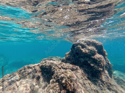 A large rock is pro-tubing from the bottom of the sea all the way to the surface in crystal clear blue waters