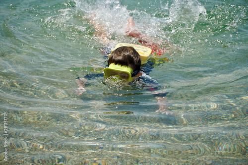Toddler snorkeling with the help of a floatation device in sallow clear sea waters.