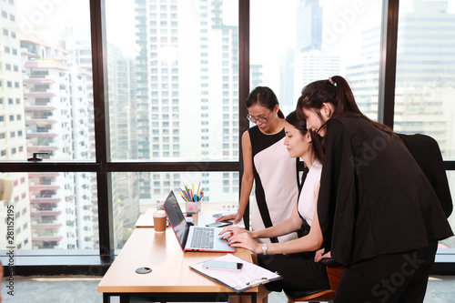 three asian colleagues businesswomen whispering or gossiping someone from internet with laughing while working at the office with computer