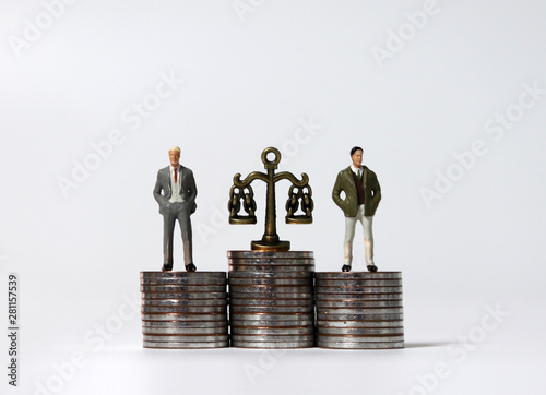 Miniature men standing on a pile of coins of the same height. Pile of coins and a miniature scale. photo