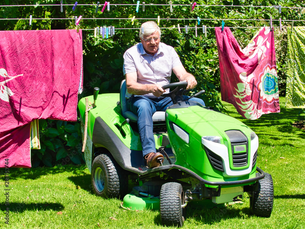 Senior man driving a tractor lawn mower in garden with flowers Senior man driving a tractor lawn mower in garden with flowers