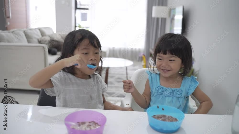 happy two little asian girls having breakfast together in the kitchen at home happy two little asian girls having breakfast together in the kitchen at home