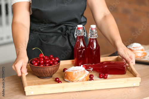 Woman with tasty cherry juice and sweet bun on tray at table
