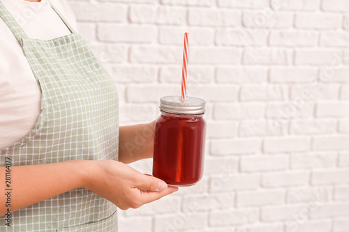 Woman with mason jar of tasty cherry juice on white brick background