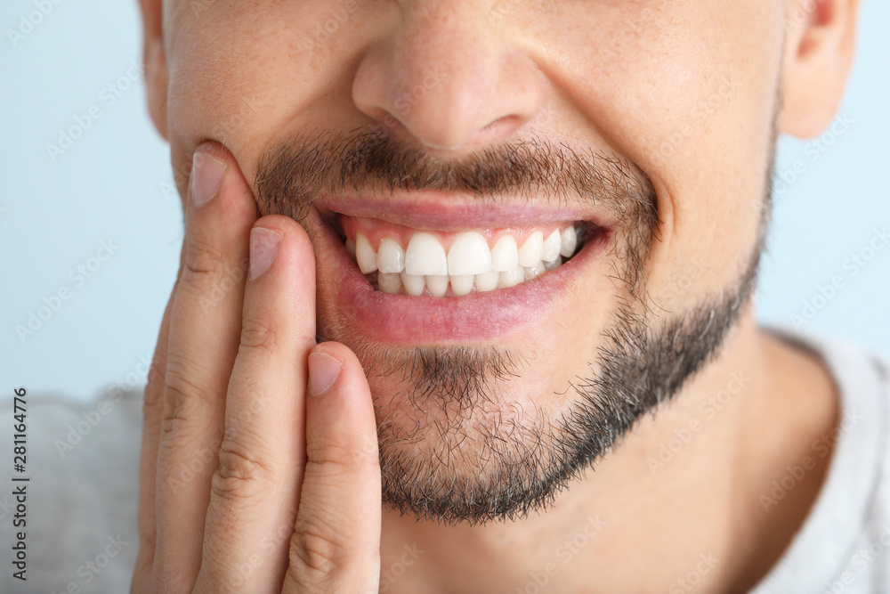 Man suffering from toothache against color background, closeup