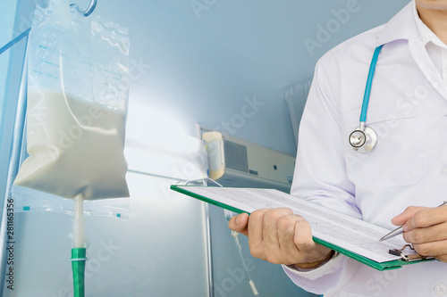 Doctor writing chart with enteral feeding bag on IV pole in hospital room background. photo