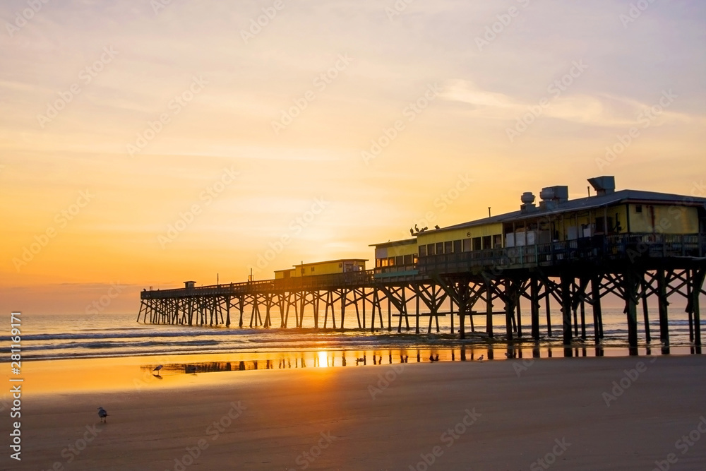 Early morning at the beach. Scenic view with sunrise over calm Atlantic ocean and wooden pier. Daytona Beach beautiful marine landscape, Florida, USA. Vacation concept.