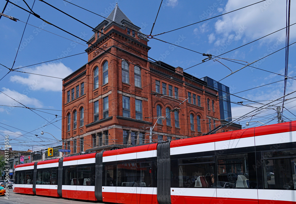  A long modern articulated streetcar goes past an old Victorian hotel building  in Toronto.