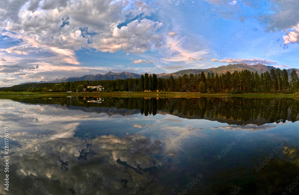 Fototapeta premium Panoramic view Columbia Lake. Beautiful reflections of mountains, trees and a vacation cottage in calm lake in the morning. Columbia lake. British Columbia. Canada